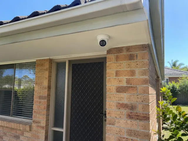 Exterior security camera mounted under eave above a brick home entry in Nerang