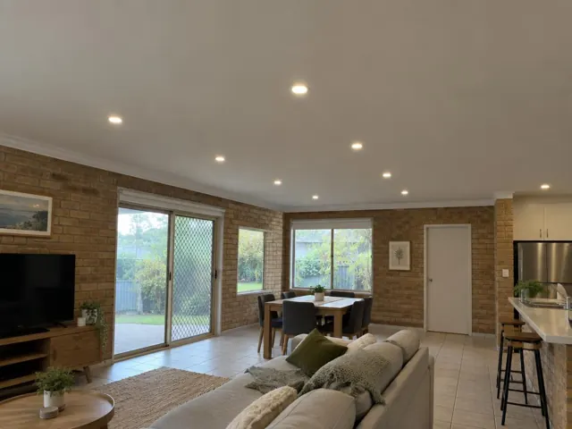Open-plan living room with recessed ceiling downlights, brick walls and tiled floor in Worongary